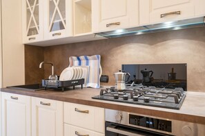 Una cocina moderna con armarios blancos, estufa a gas, cafetera y escurreplatos.