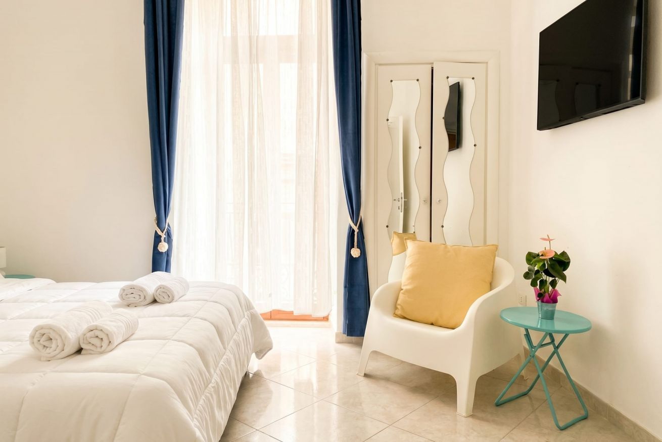 A hotel room with a bed, a chair, a small table with a plant, and a TV mounted on the wall.