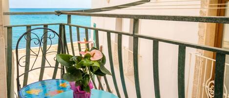 A balcony with a table, a chair, a potted plant, and a view of the sea.
