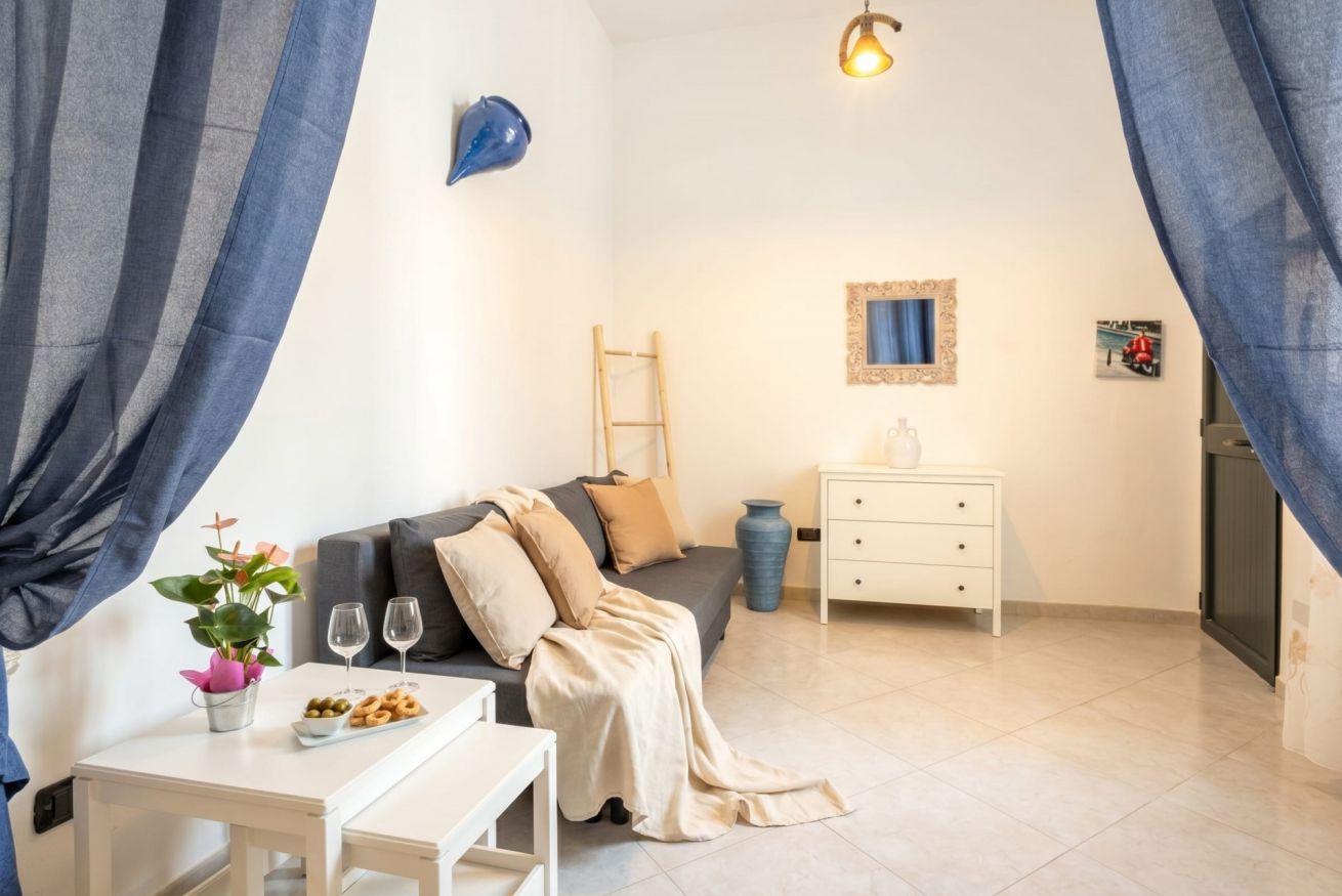 A modern room with a sofa, a small table with a plant and snacks, a white dresser, and a ladder against the wall.