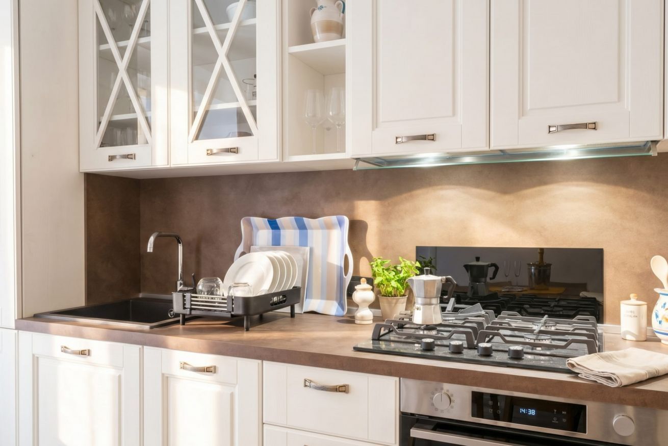 Una cucina moderna con mobili bianchi, un fornello a gas, una macchina da caffè e un espositore per piatti.