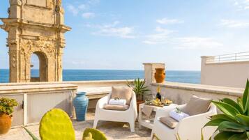 Eine Terrasse mit weißen Stühlen, einem Tisch mit Speisen und Getränken, einer großen Vase und einer Kakteepflanze.