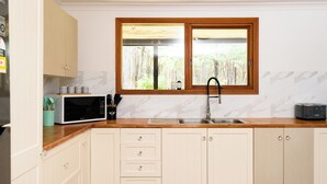 A kitchen with a wooden countertop, a sink, a window with a view of trees, and a microwave. - La Moneta Retreat – A Sanctuary for Healing & Hope -Tranquil Hillside Haven (Dean)