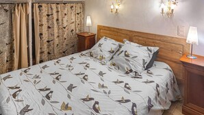 A bedroom with a bed featuring a bird pattern, wooden headboard, two bedside tables with lamps, and a curtain with a bird pattern. - Beautiful home in La Tour-d'Aigues with swimming pool (La Tour-d'Aigues)