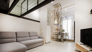 A modern living room with a grey sofa, a dining area with a table and chairs, and a TV on a wooden stand. - Palazzo D’Amelj – Modern Loft in the Heart of Bari Vecchia (Bari)