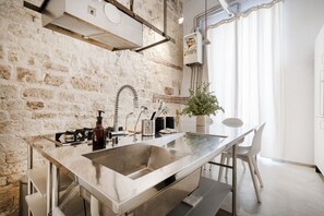 A modern kitchen with a large island, stainless steel appliances, and a brick wall.