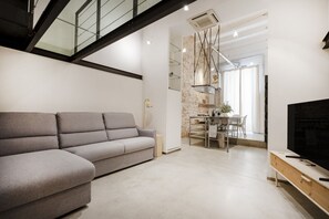 A modern living room with a grey sofa, a dining area with a table and chairs, and a TV on a wooden stand.