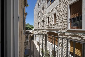 Un callejón estrecho con edificios de piedra, una barandilla metálica y un cielo azul despejado.