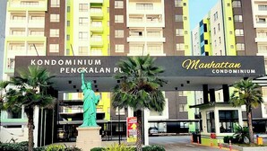 A condominium complex with a prominent entrance sign, a statue, and multiple buildings with balconies.