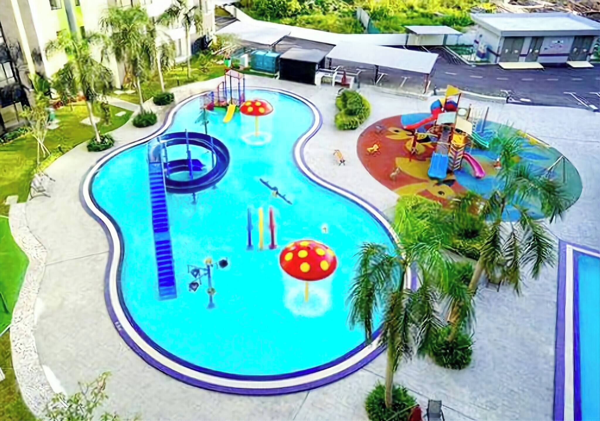 A swimming pool with a slide, a children's play area, and palm trees.