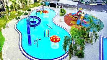A swimming pool with a slide, a children's play area, and palm trees.