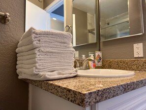A bathroom with a granite countertop, a sink, and a stack of white towels.