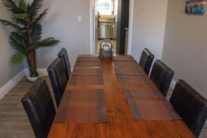 A dining room with a long wooden table, black chairs, and a potted plant.