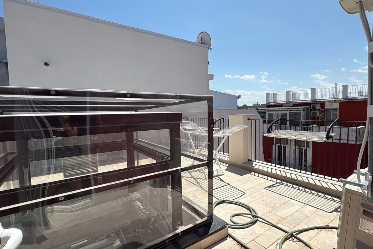 Una terrazza panoramica sul tetto con ringhiera in vetro, arredi da esterno e vista sugli edifici circostanti.