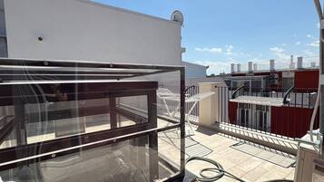 Una terrazza panoramica sul tetto con ringhiera in vetro, arredi da esterno e vista sugli edifici circostanti.