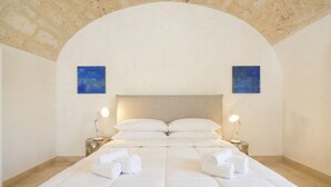A neatly made bed with white linens and towels, two bedside lamps, and two blue paintings on the walls. - Palazzo della Torre 001 - Historical modern stay (Bari)