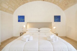 Una cama bien hecha con ropa y toallas blancas, dos lámparas de noche y dos cuadros azules en las paredes.