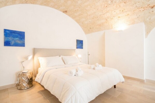 A bedroom with a bed, bedside lamps, a round side table, and two wall-mounted paintings.