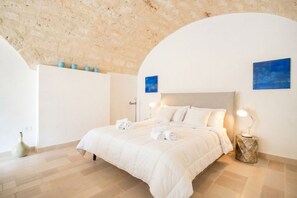 Een slaapkamer met een bed, nachtlampjes, een vaas en een blauw schilderij aan de muur.