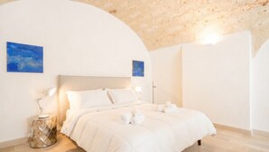A bedroom with a bed, bedside lamps, a round side table, and two wall-mounted paintings.