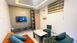 A modern living room with a flat-screen TV mounted on the wall, a sofa, a coffee table, and a chair. - Humble Citadel Hotel (Lagos)