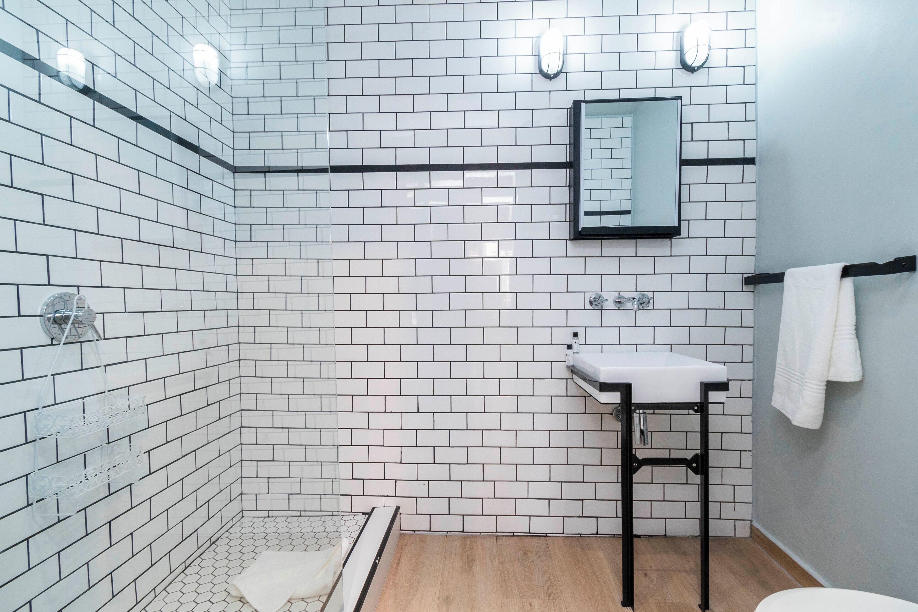 Un baño con azulejos blancos tipo metro, un lavabo blanco, un perchero y una zona de ducha.