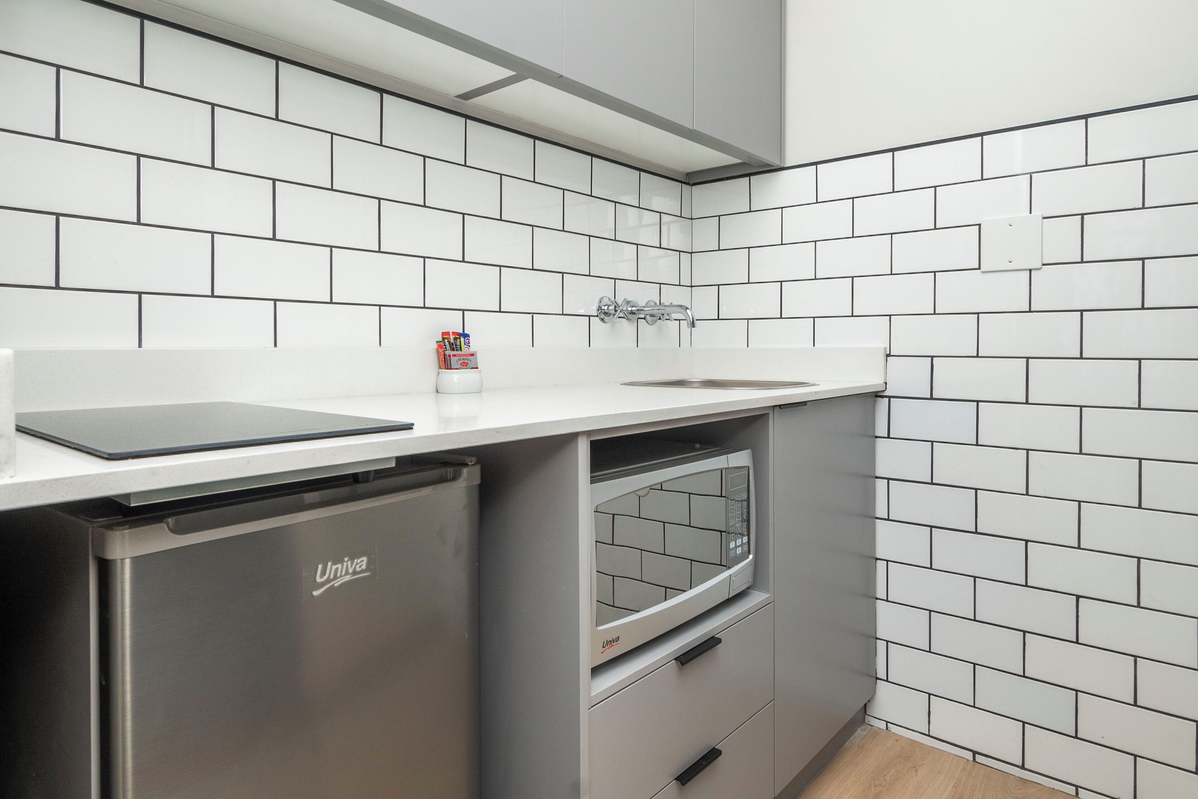 Une cuisine compacte avec des carreaux de métro blancs, un lave-vaisselle encastré et un four à micro-ondes.