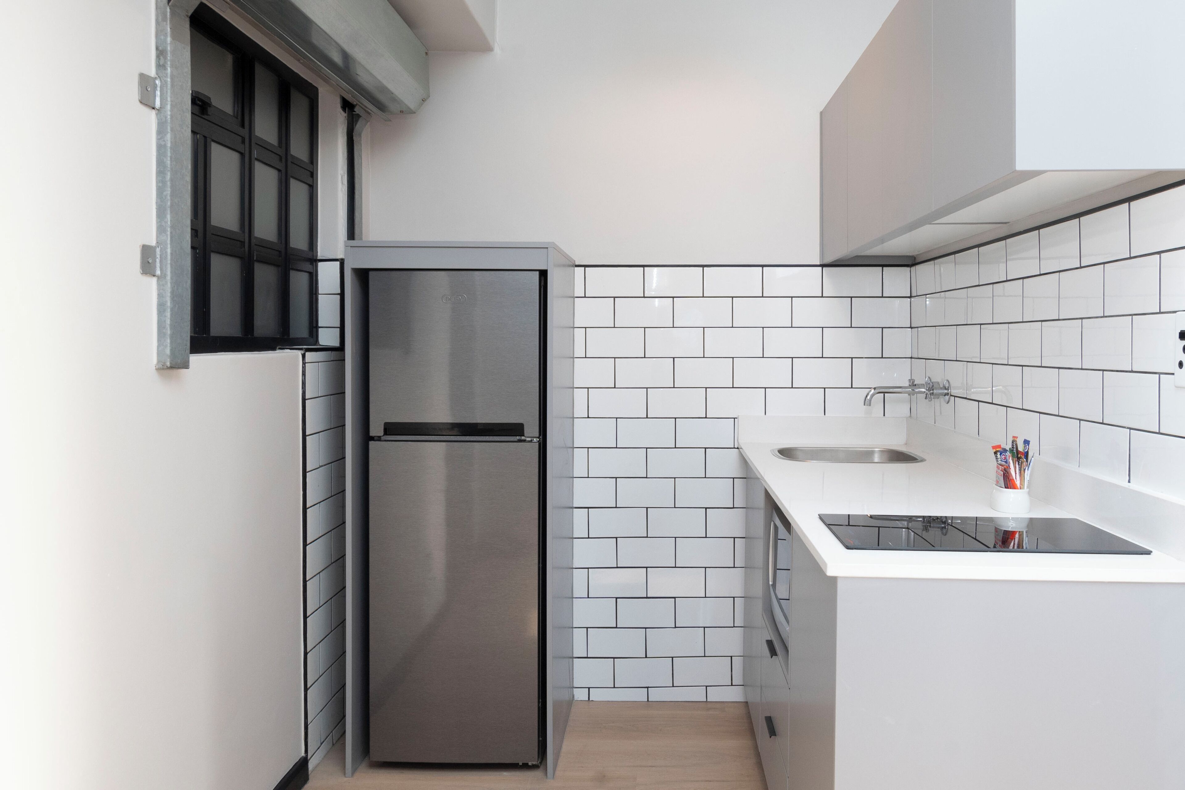 A compact kitchen with white tiles, a stainless steel refrigerator, and a sink.