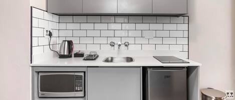 Una cocina compacta con microondas, un refrigerador pequeño, un lavamanos y una tetera.
