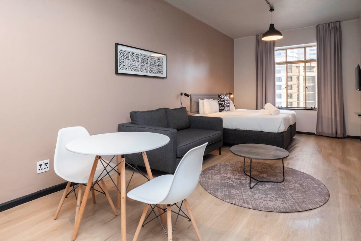 Una habitación de hotel moderna con una cama, un sofá, una mesa de comedor con sillas y una mesita auxiliar.