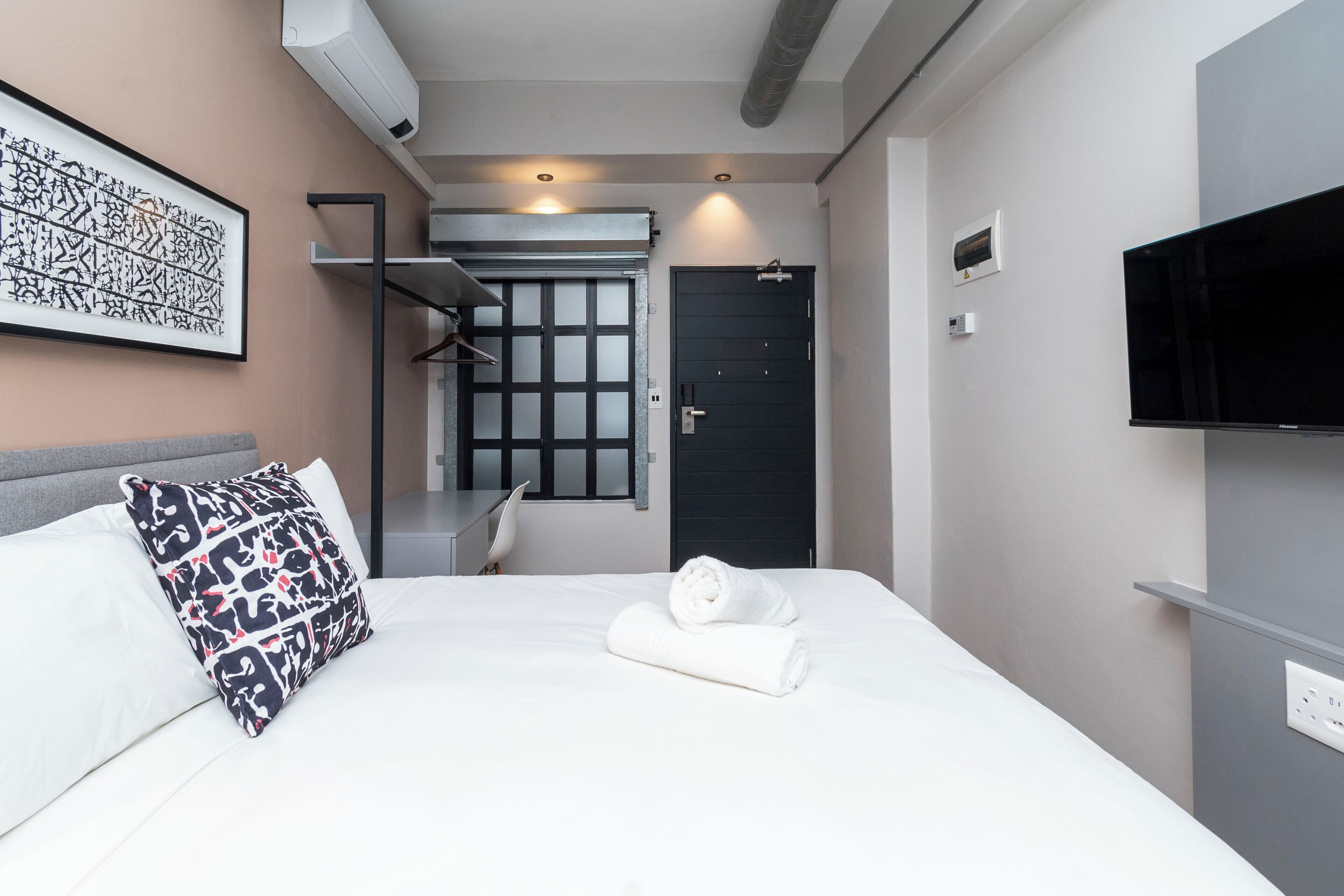 Moderni hotellihuone, jossa on siististi pedattu sänky, taulutelevisio ja suuri ikkuna.