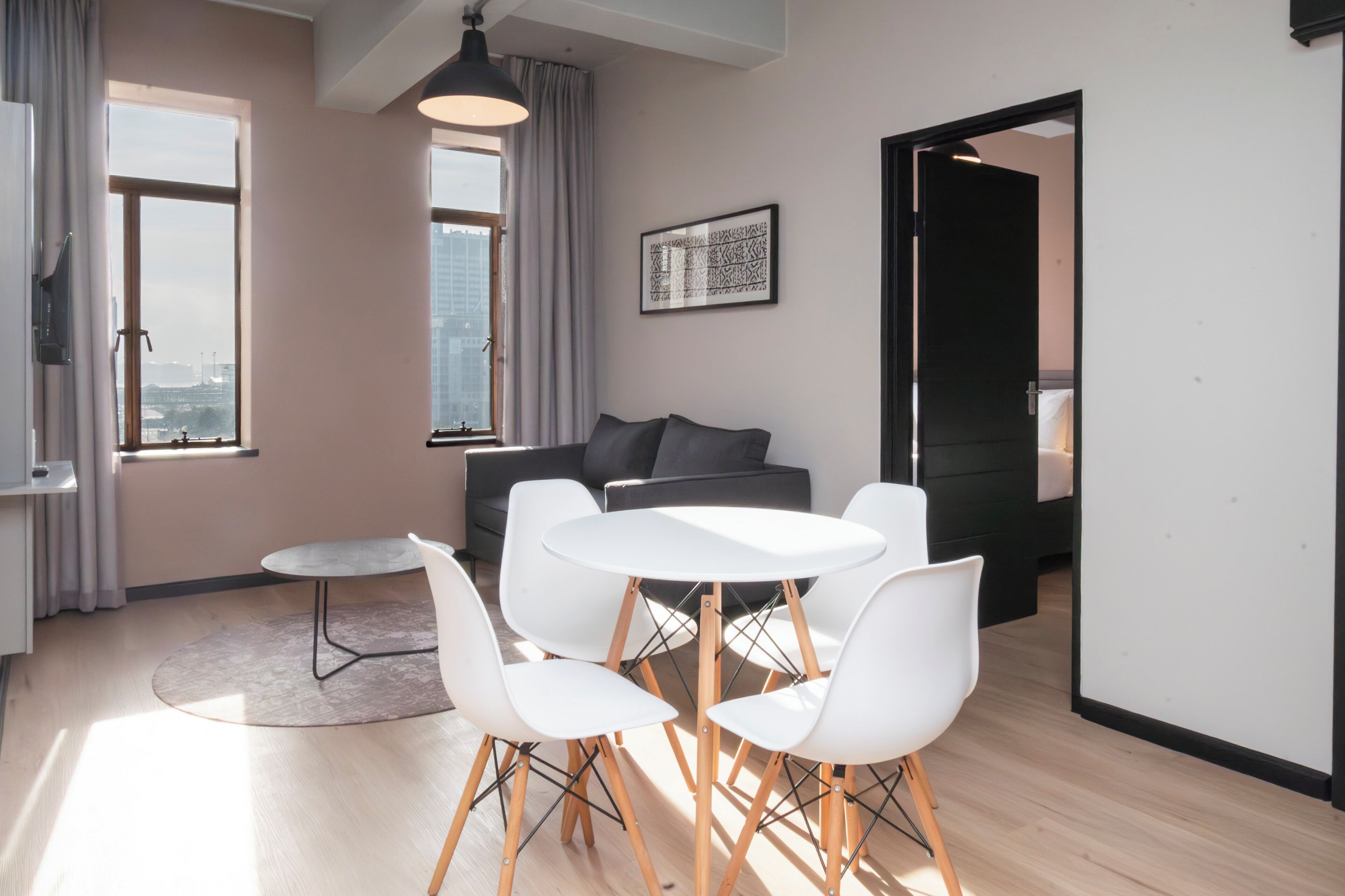 A modern living room with a sofa, a dining table with chairs, and a large window offering a city view.
