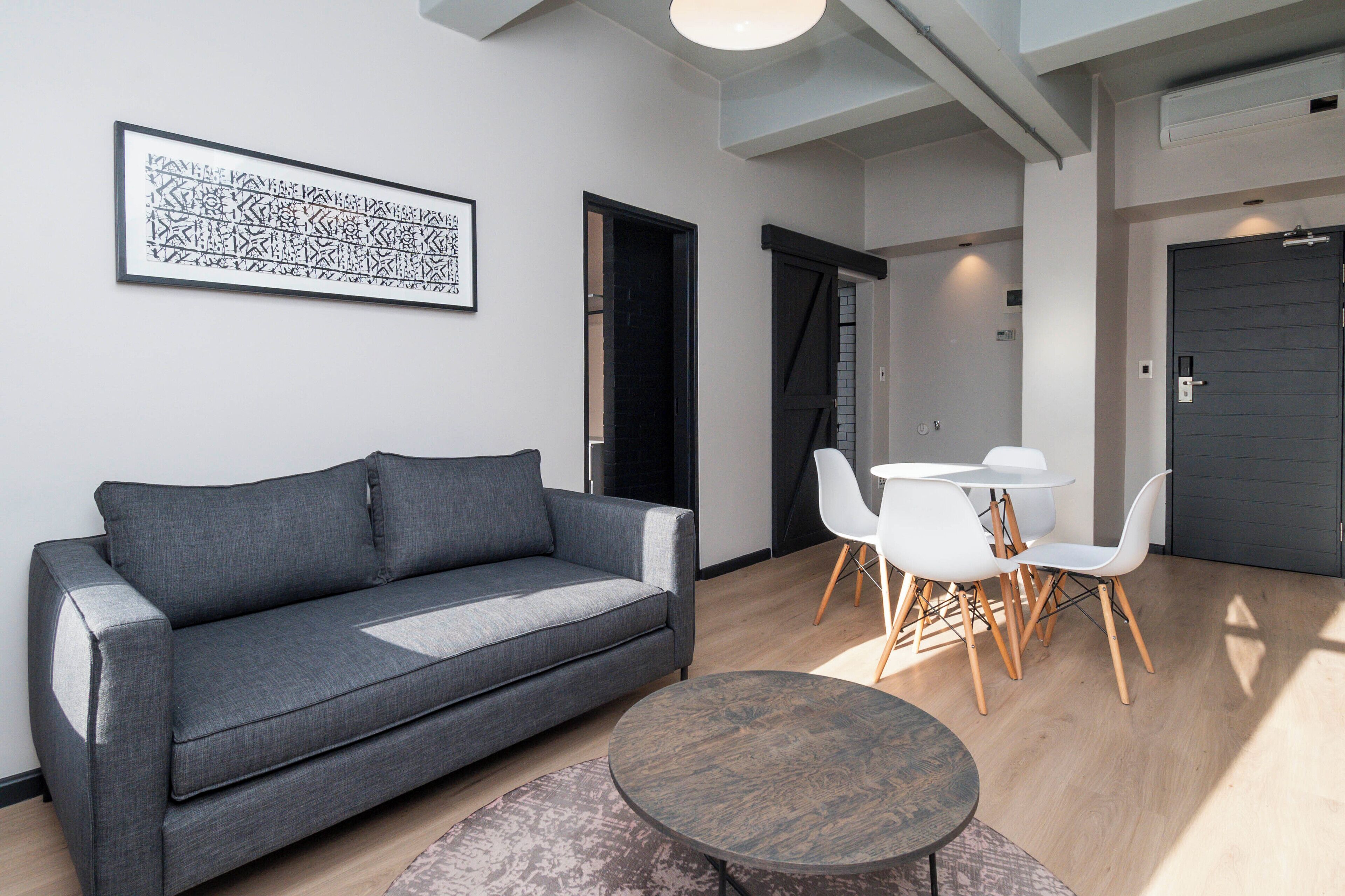 A modern living room with a grey sofa, a round coffee table, and a dining area with white chairs and a small table.