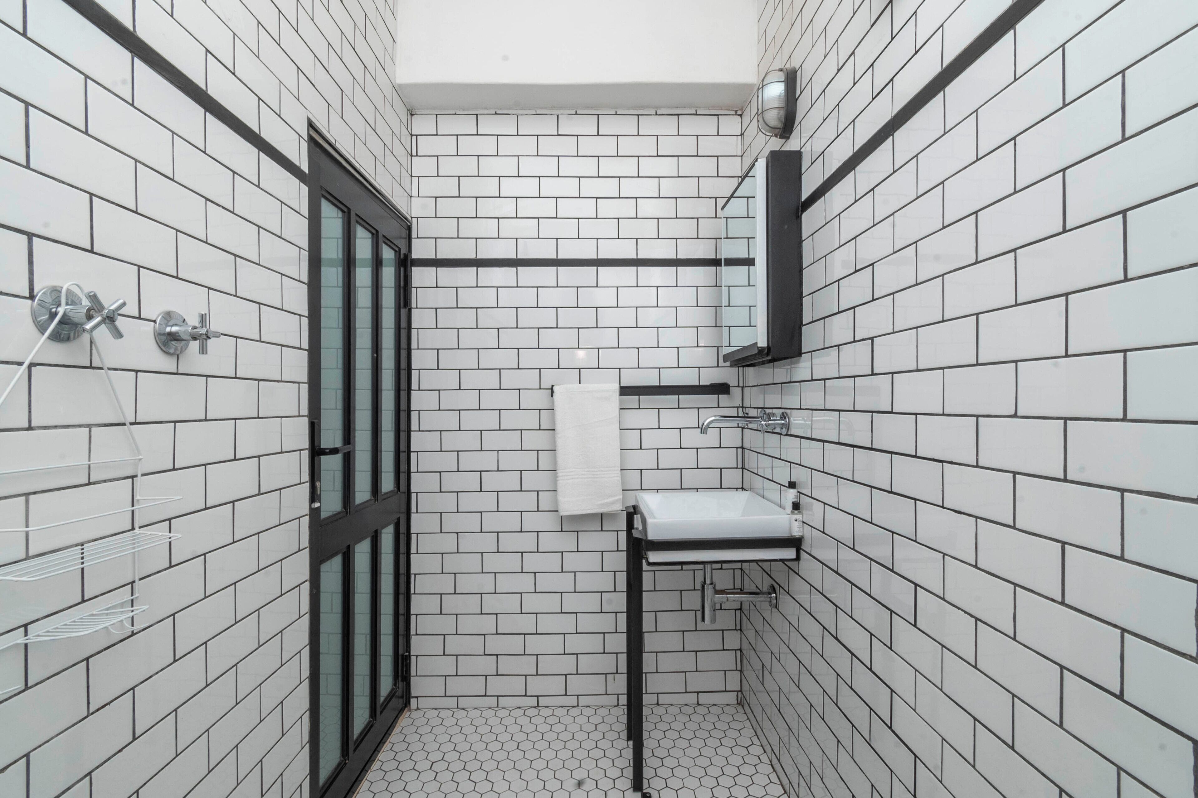 A bathroom with white tiled walls, a black-framed glass door, a white sink, and a towel hanging on the wall.