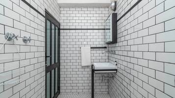 A bathroom with white tiled walls, a black-framed glass door, a white sink, and a towel hanging on the wall.