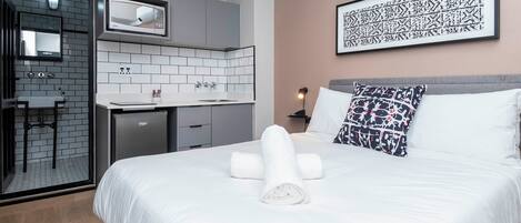 A modern hotel room with a bed, a desk, and a kitchenette.