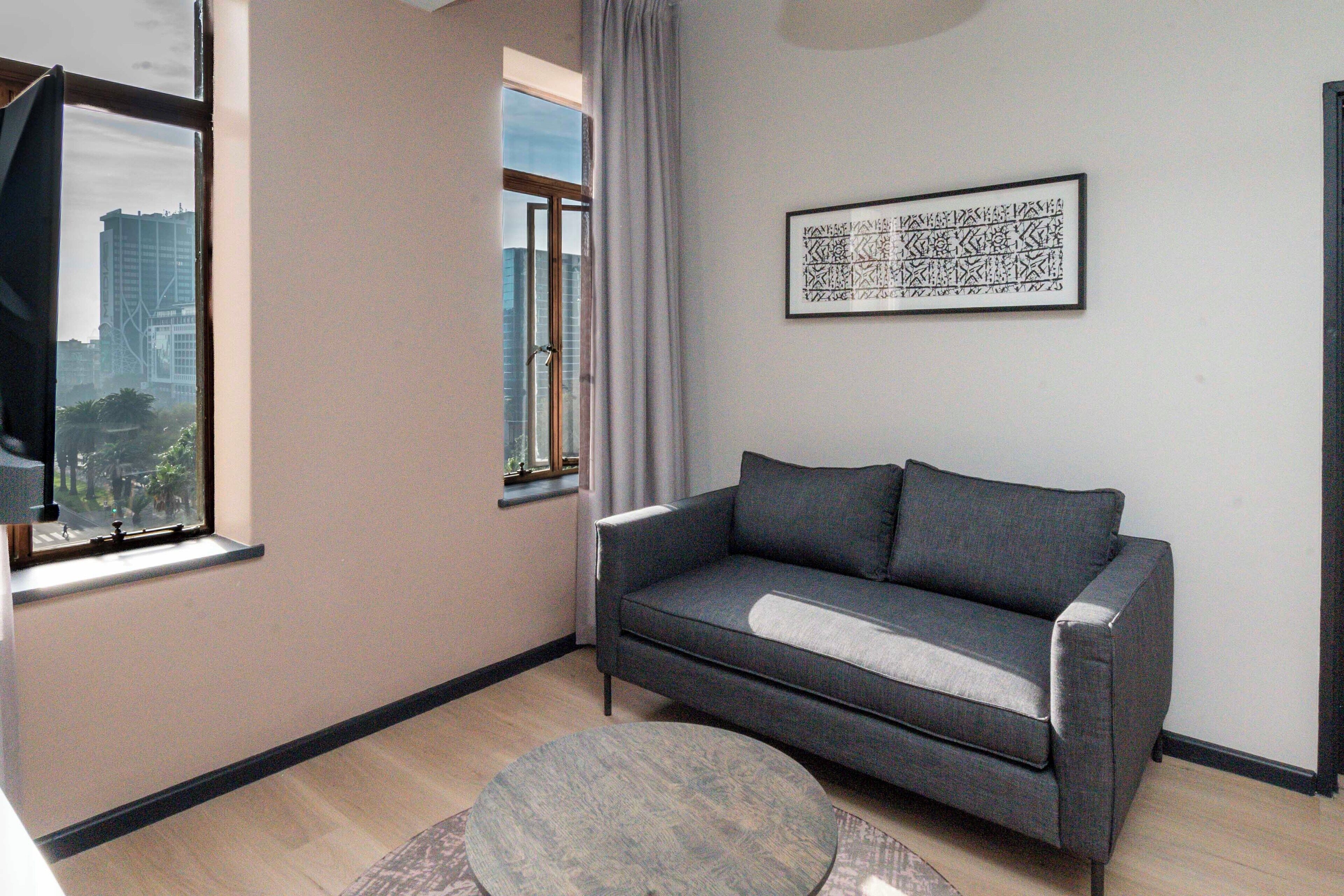 Un salon moderne avec un canapé gris, une table basse ronde et une œuvre d’art abstraite encadrée accrochée au mur.