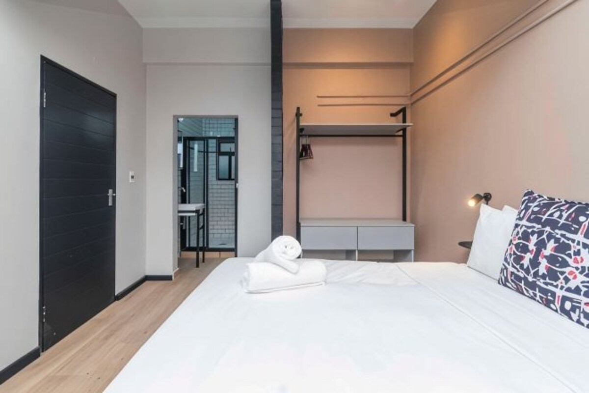 Ett modernt hotellrum med en säng, ett sängbord och en garderob.