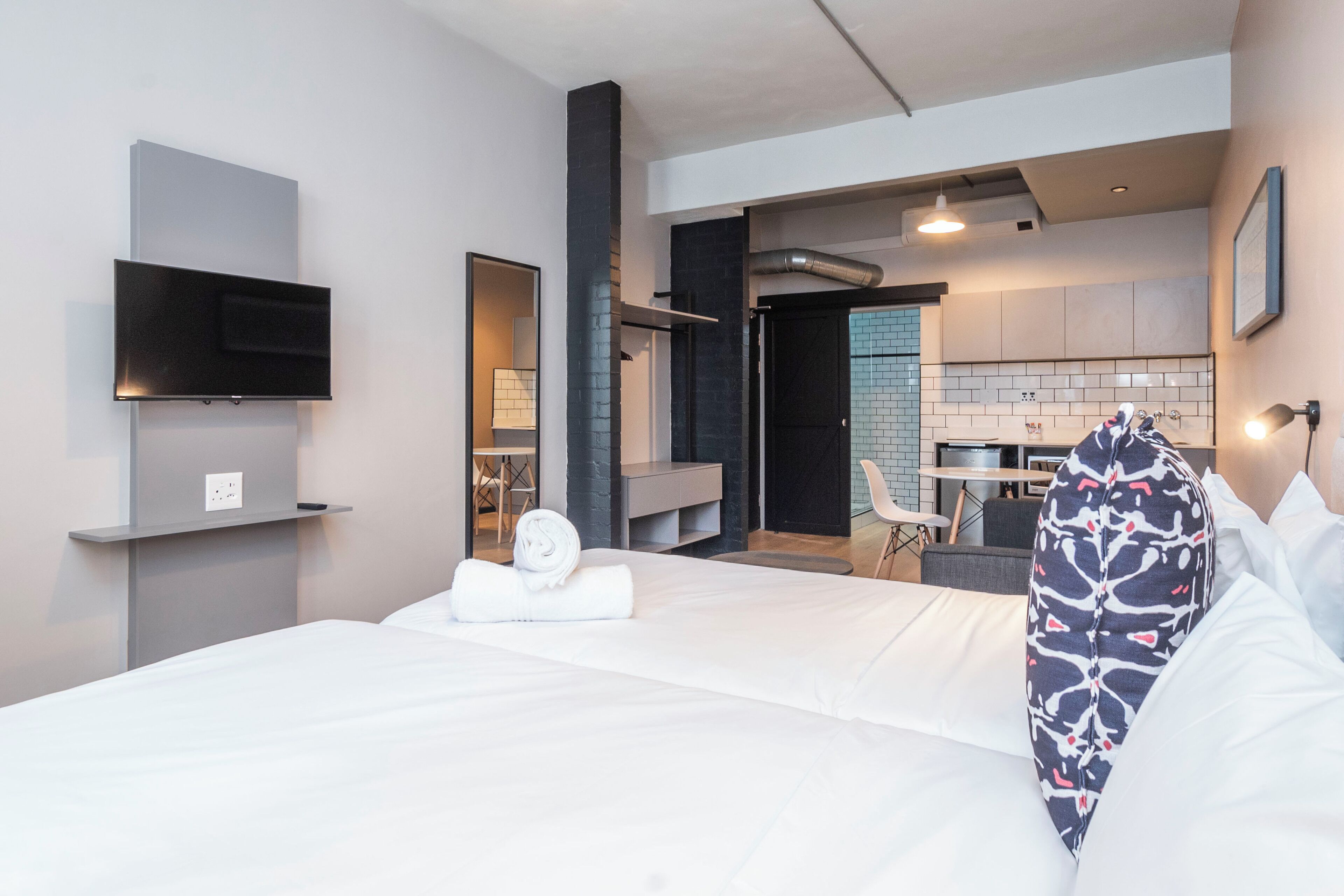 Una habitación de hotel moderna con una cama grande, un televisor de pantalla plana montado en la pared y una kitchenette al fondo.