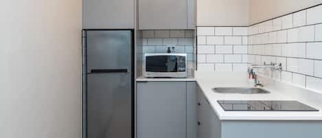 A compact kitchen with a stainless steel refrigerator, a microwave, and a sink with a faucet.