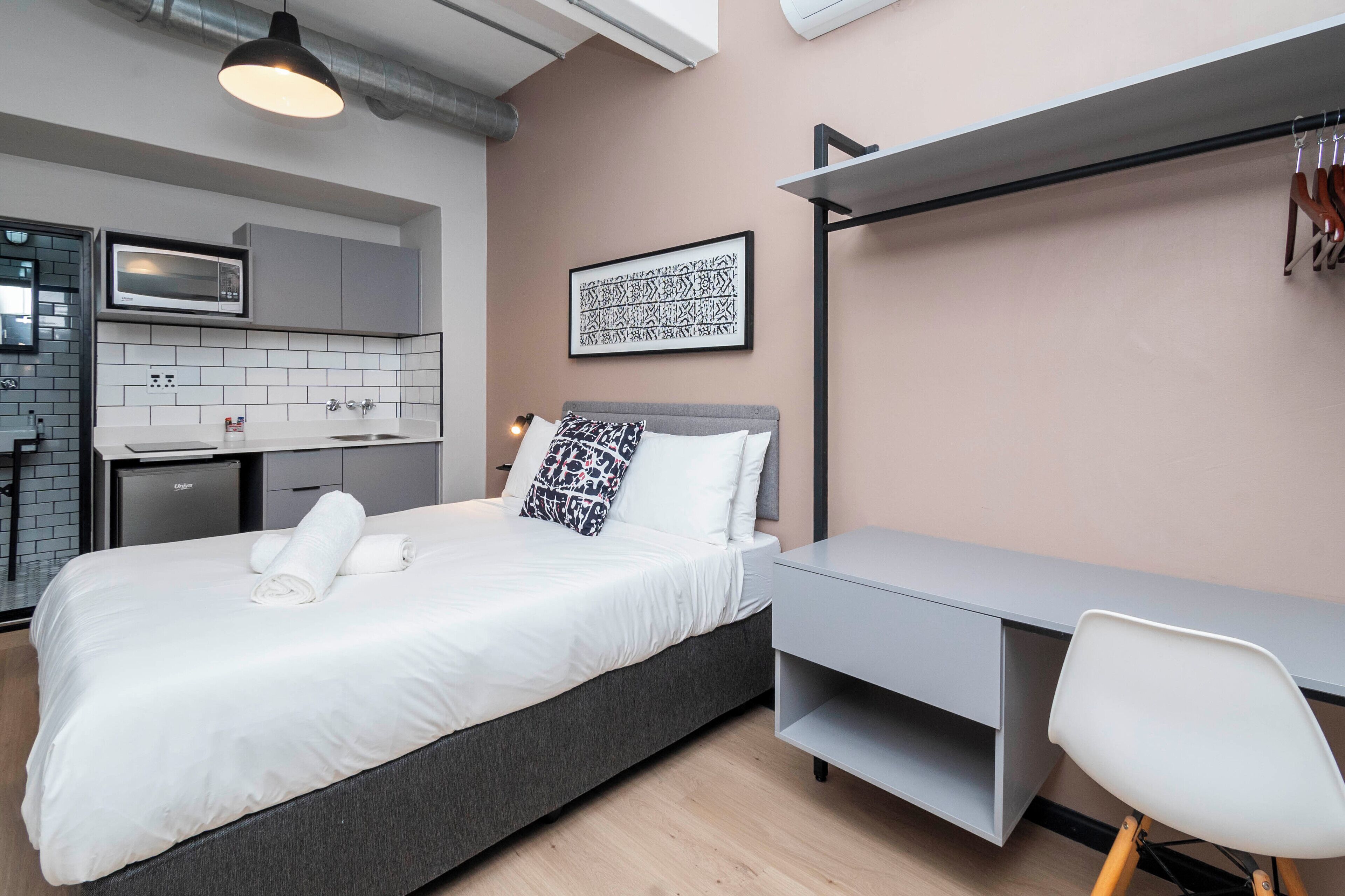 A modern room with a bed, a desk, and a kitchenette.