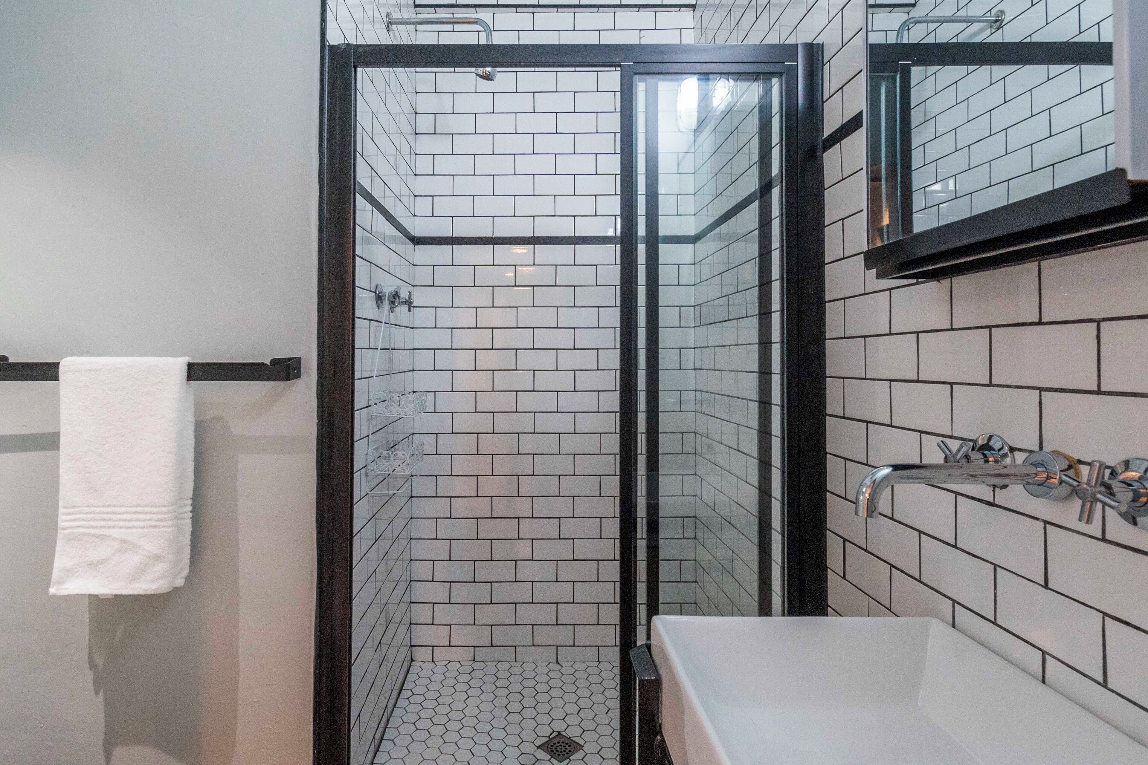 A modern bathroom with a glass-enclosed shower, white tiled walls, and a white sink with a chrome faucet.