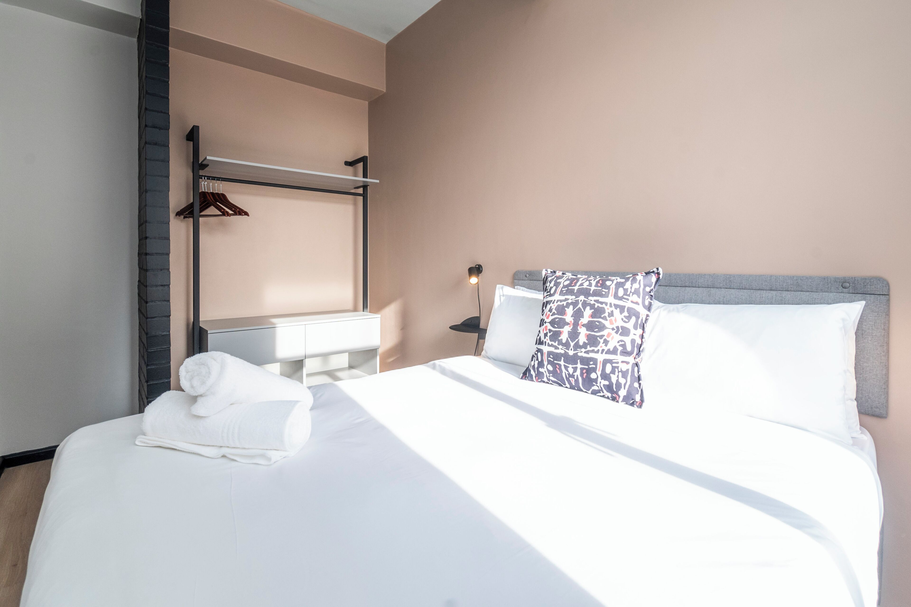 A neatly made bed with white linens, a hanging towel, and a pillow with a patterned cover.