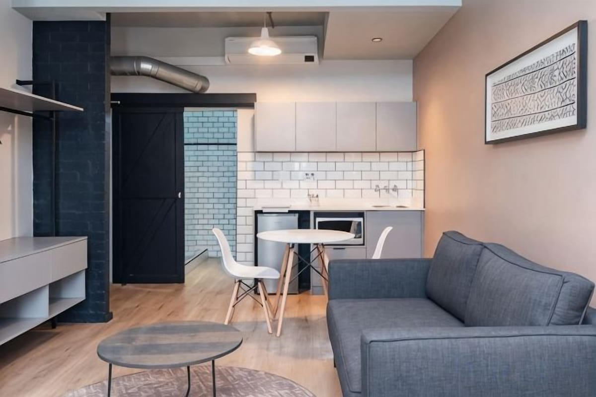 A modern kitchen with white cabinets, a dining area with a gray sofa and chairs, and a small round table.