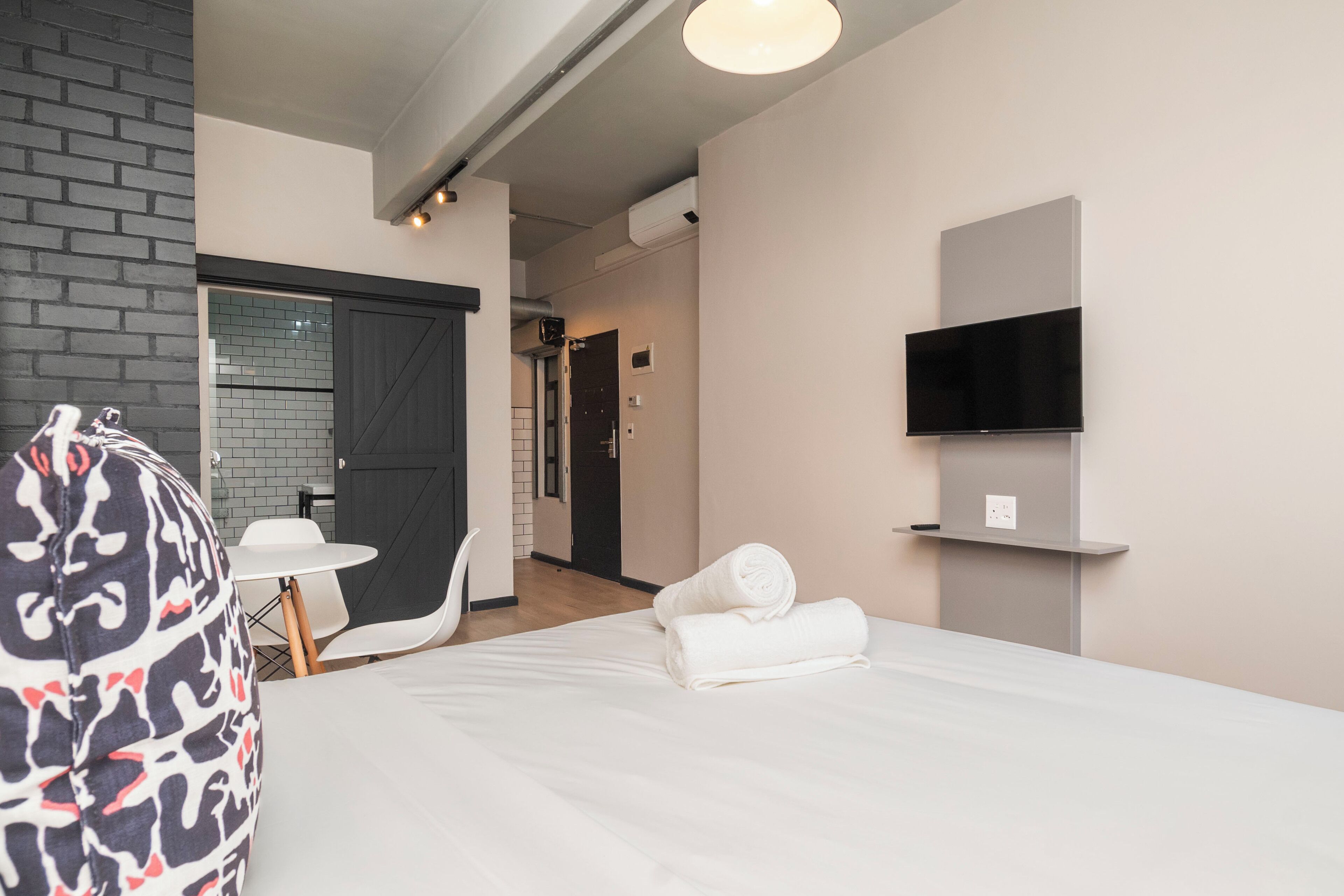 Una camera d'albergo con un letto, una televisione a parete, un tavolino e una sedia.