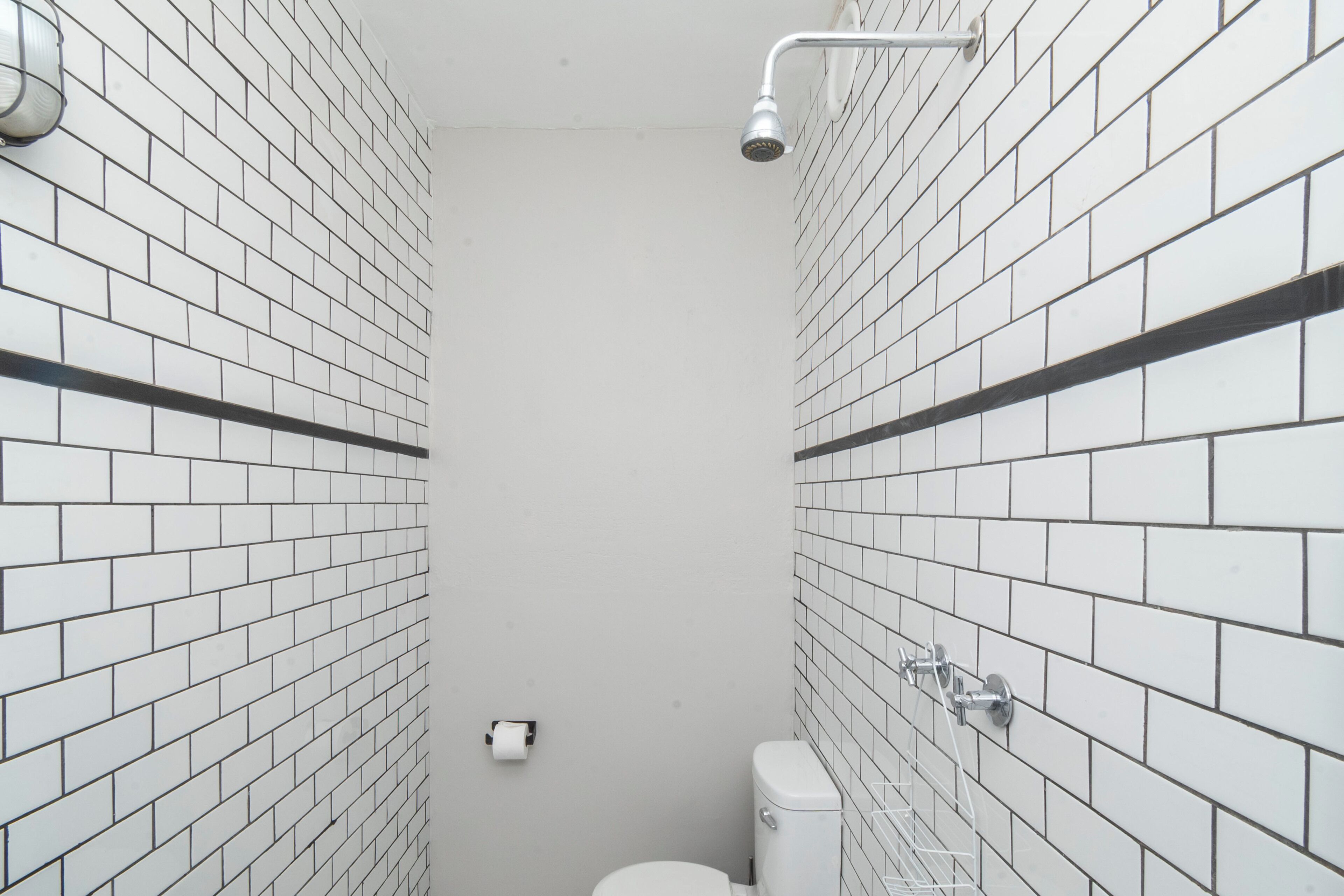 A narrow bathroom with white tiled walls and a white toilet.
