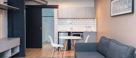 A modern living space with a grey sofa, a small round table, and a kitchen area with white cabinets and a microwave.