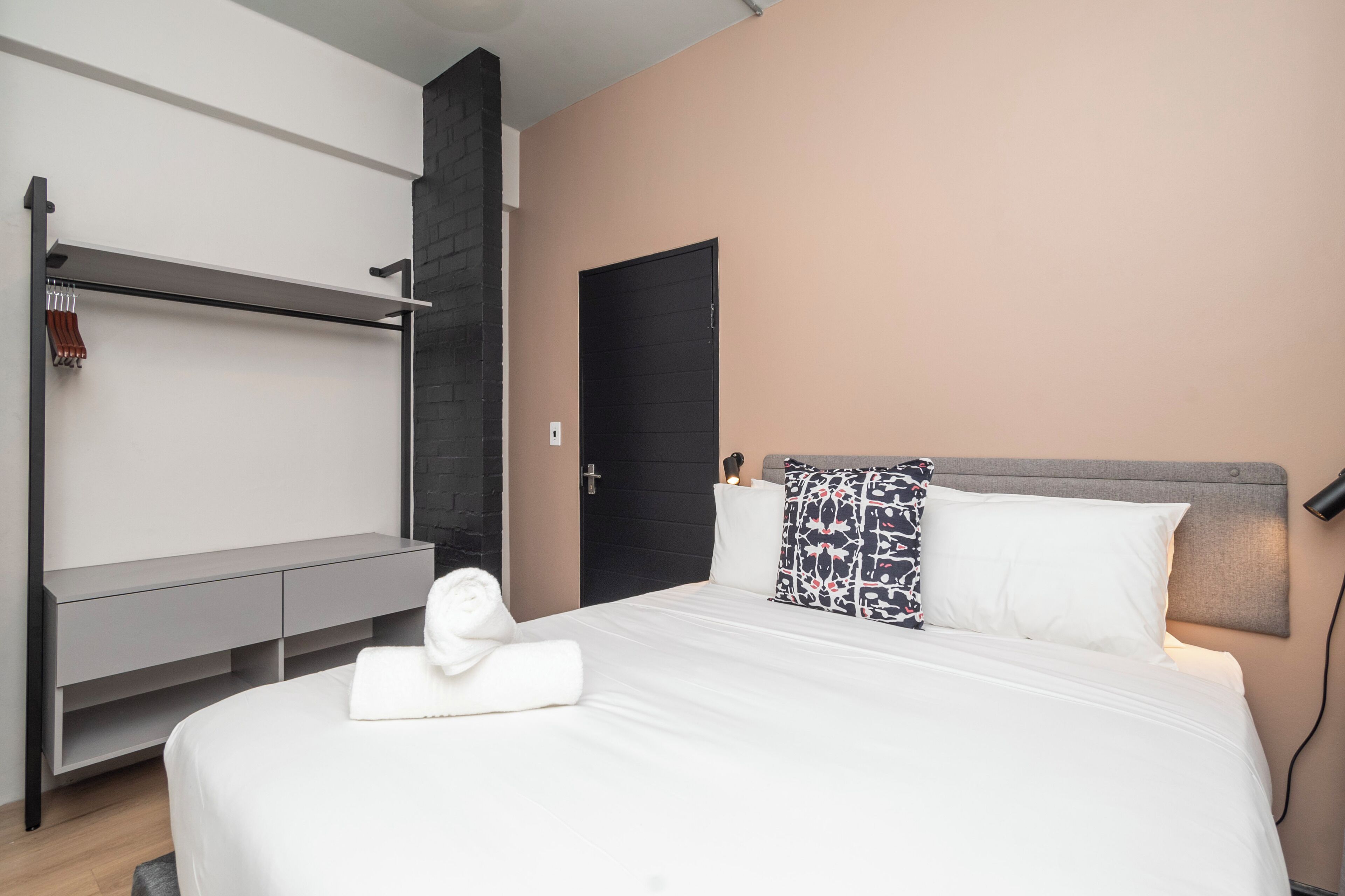 Een moderne hotelkamer met een bed, een grijze console, een zwarte deur en een aan de muur bevestigde handdoekhouder.