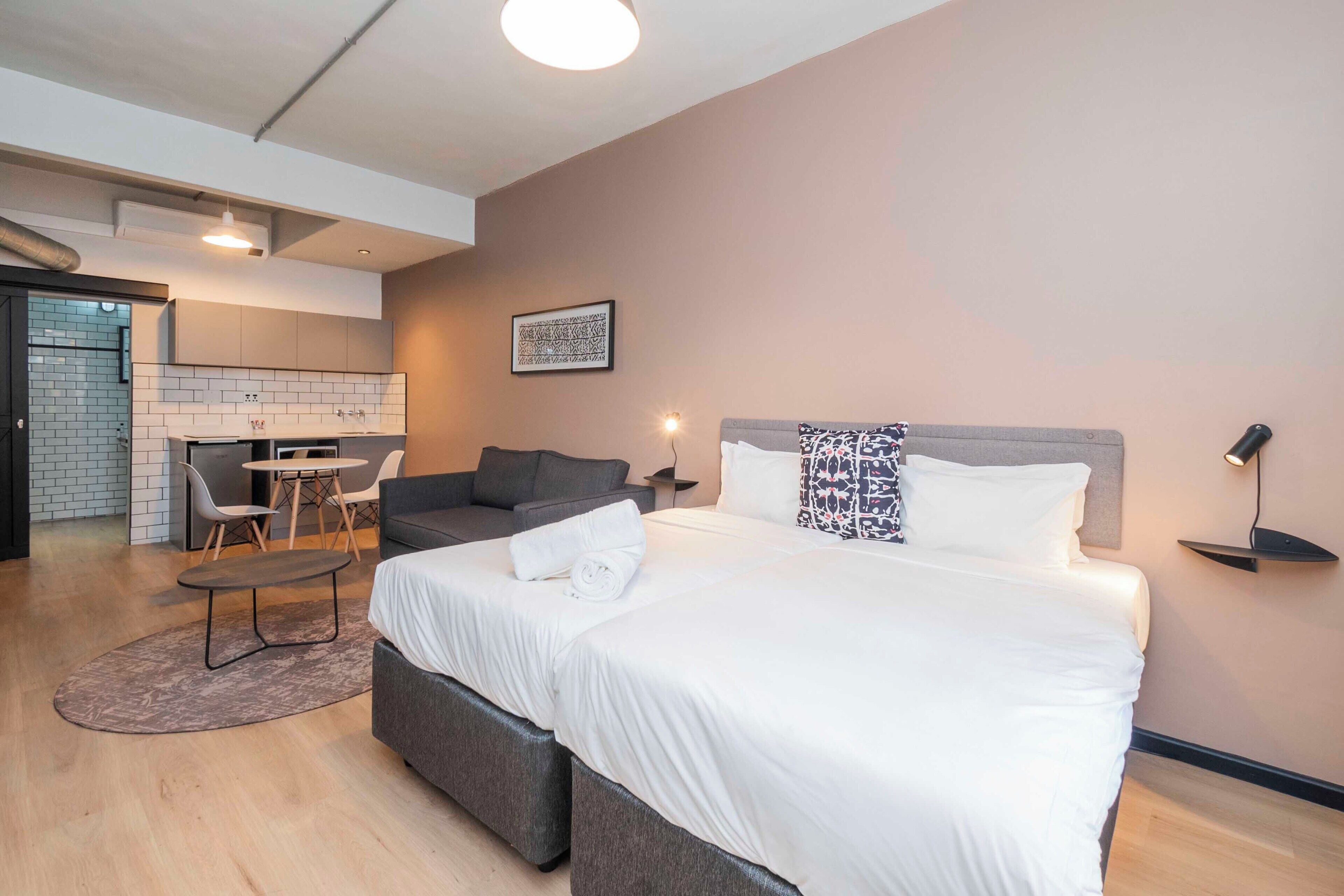 Una camera d'albergo moderna con un letto grande, una poltrona, un piccolo tavolo da pranzo e un angolo cottura sullo sfondo.