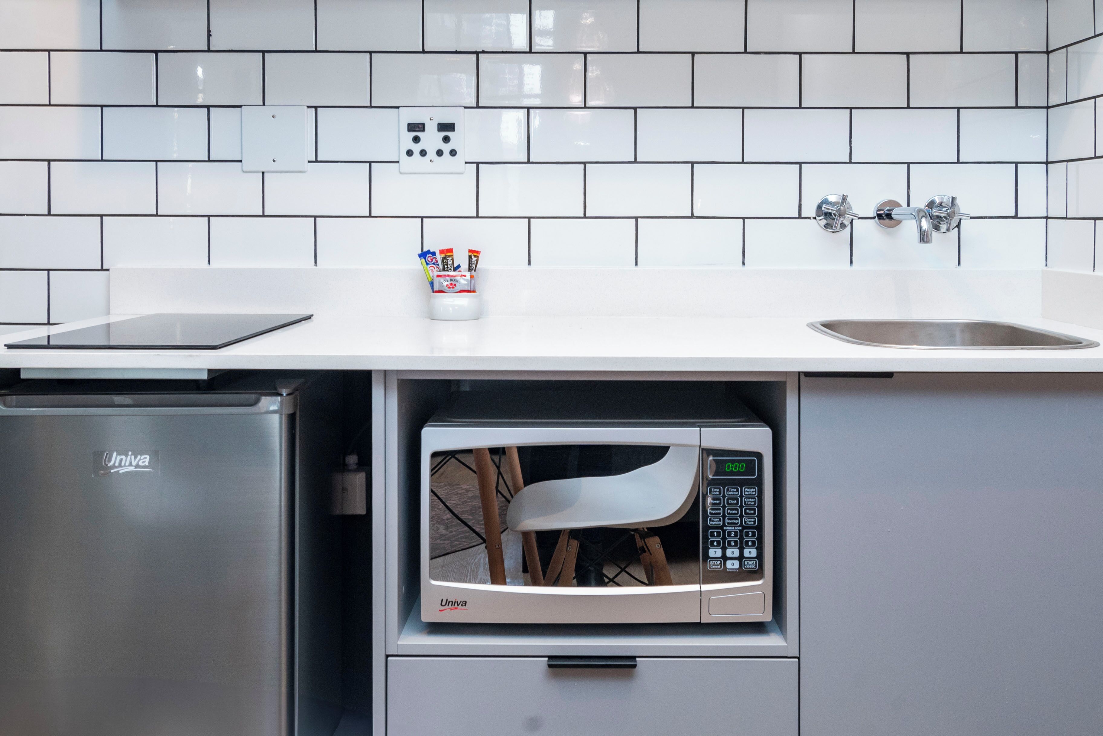 Een kleine keuken met een ingebouwde magnetron, een kleine koelkast en een spoelbak.